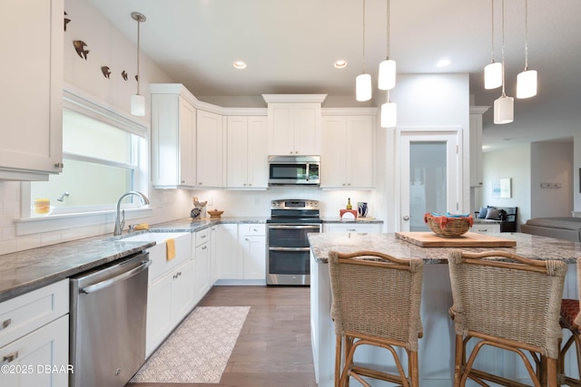 kitchen with white cabinets, a kitchen bar, appliances with stainless steel finishes, and decorative light fixtures