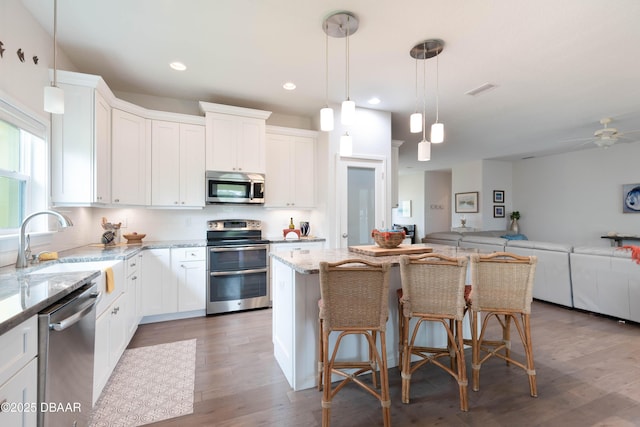 kitchen with appliances with stainless steel finishes, a center island, white cabinetry, a kitchen breakfast bar, and light stone countertops