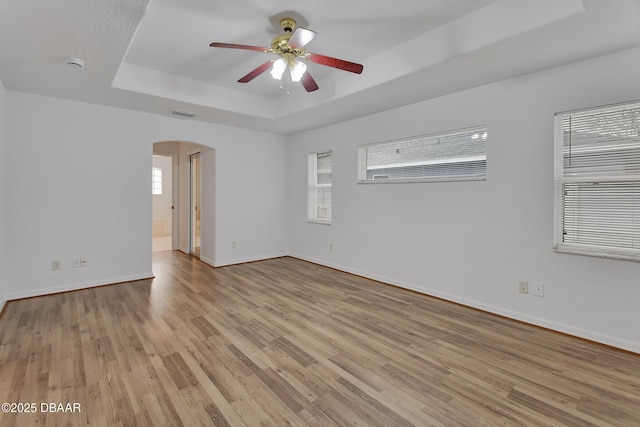 spare room featuring arched walkways, baseboards, a raised ceiling, and light wood-style floors