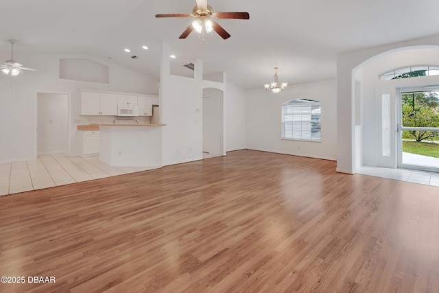 unfurnished living room with a wealth of natural light, light wood-style floors, high vaulted ceiling, and ceiling fan with notable chandelier