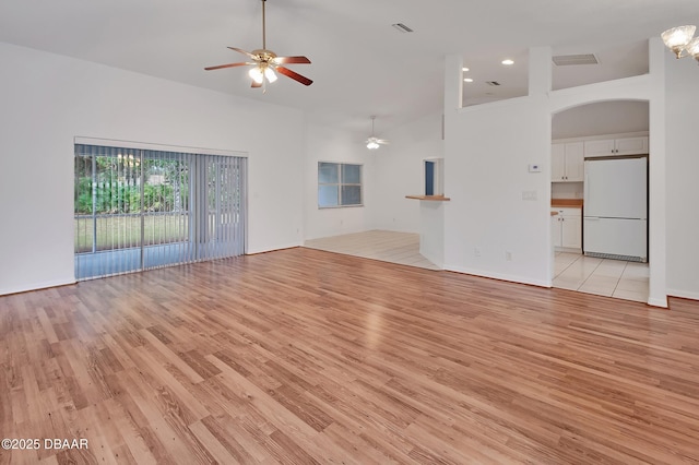 unfurnished living room with visible vents, ceiling fan with notable chandelier, a high ceiling, and light wood-style floors