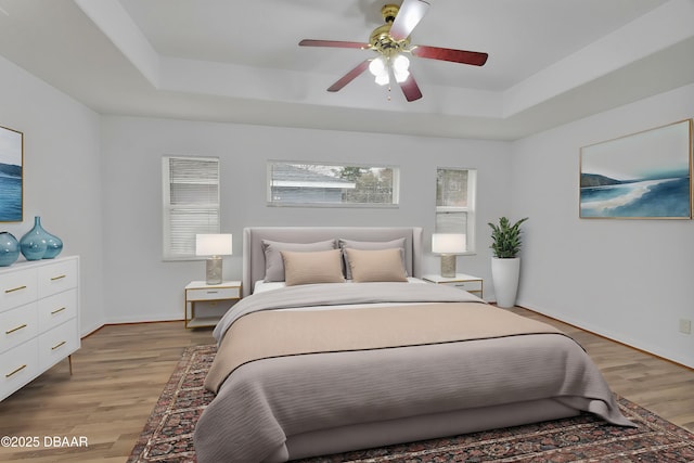 bedroom with ceiling fan, baseboards, light wood-style floors, and a tray ceiling
