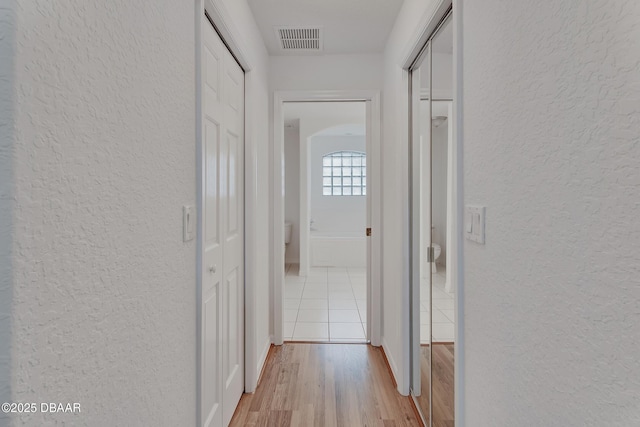 corridor with visible vents, light wood-style flooring, and a textured wall