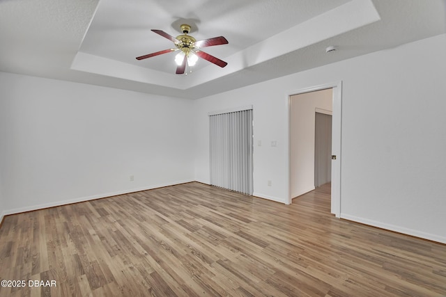 unfurnished bedroom with a tray ceiling, light wood-style flooring, a ceiling fan, and baseboards
