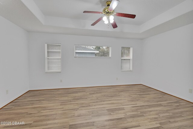 empty room featuring ceiling fan, baseboards, light wood-style floors, and a tray ceiling
