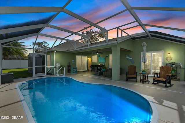 pool at dusk with a lanai, a patio area, and ceiling fan