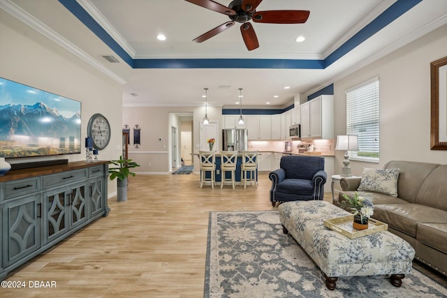 living room with ceiling fan, a raised ceiling, light hardwood / wood-style flooring, and crown molding