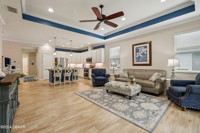 living room featuring ornamental molding, light hardwood / wood-style floors, a healthy amount of sunlight, and a raised ceiling