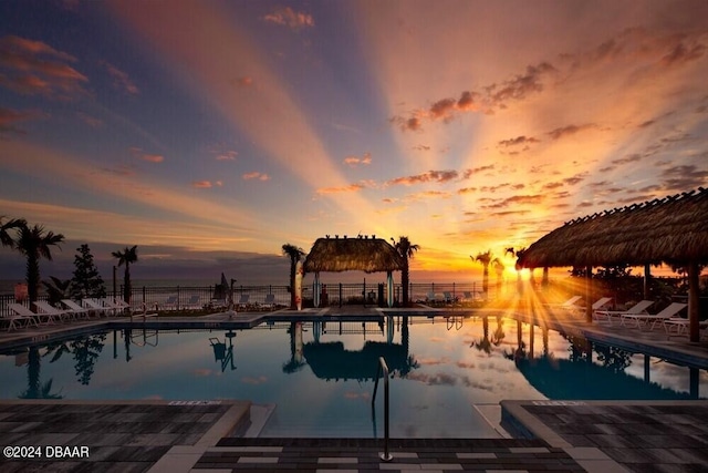 pool at dusk with a patio area, a water view, and a gazebo