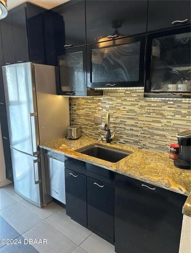 kitchen with light stone counters, sink, stainless steel refrigerator, and tasteful backsplash