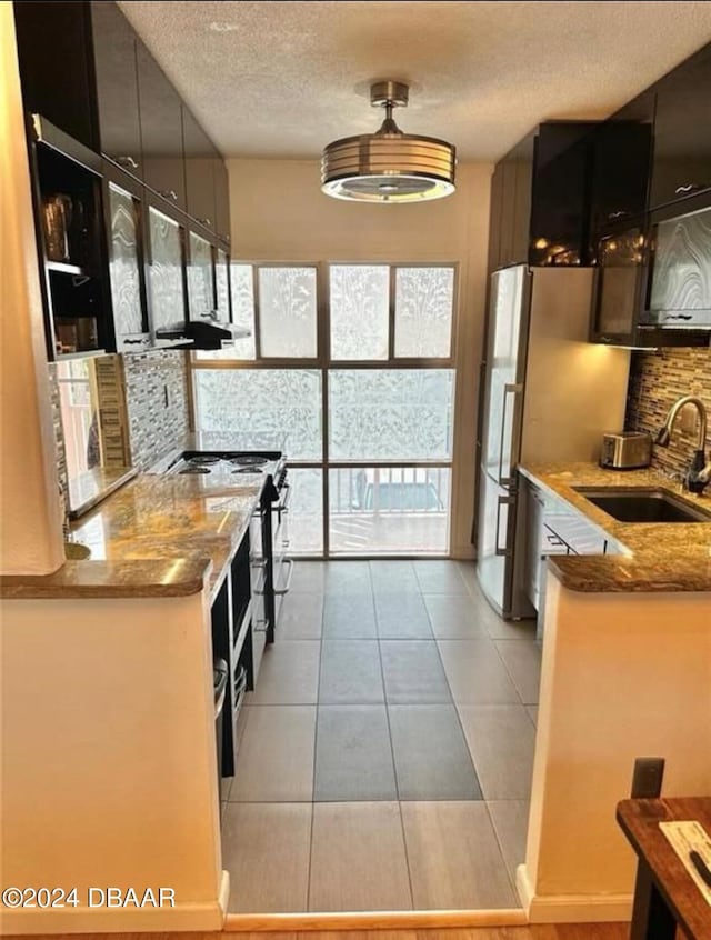 kitchen featuring sink, stainless steel stove, light stone countertops, a textured ceiling, and tasteful backsplash