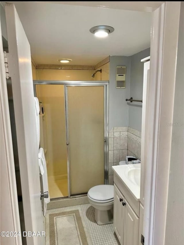 bathroom featuring toilet, vanity, tile patterned floors, and a shower with door