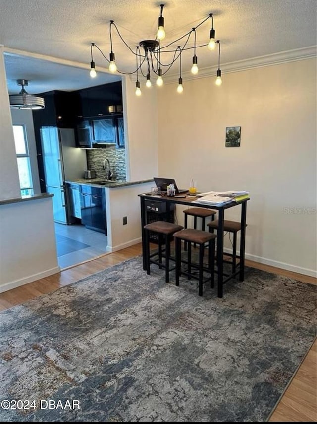 dining room with a textured ceiling, hardwood / wood-style flooring, ornamental molding, and sink