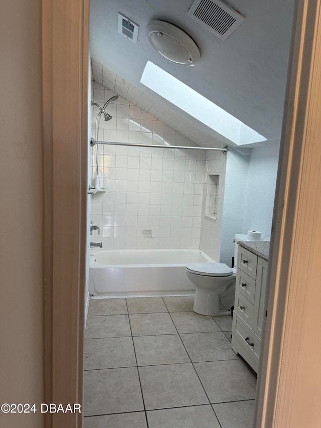 full bathroom featuring a skylight, vanity, tiled shower / bath combo, tile patterned flooring, and toilet