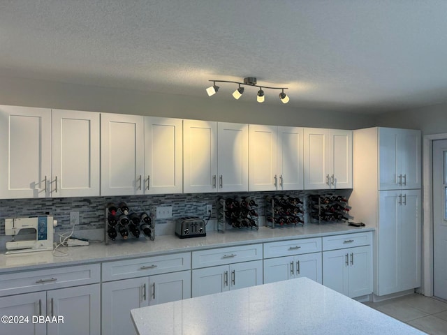 kitchen with tasteful backsplash, white cabinetry, light tile patterned floors, and a textured ceiling