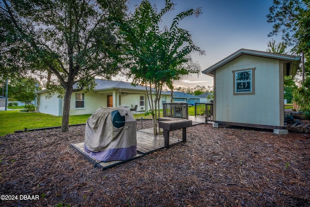 back house at dusk featuring a lawn, a shed, and a deck