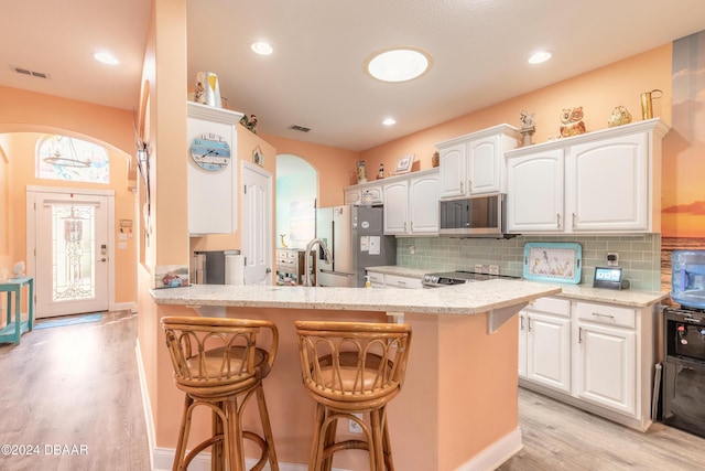 kitchen with a breakfast bar, light wood-type flooring, white cabinetry, and appliances with stainless steel finishes