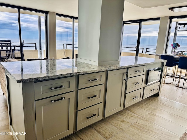 kitchen with a water view, a center island, gray cabinetry, and light stone countertops