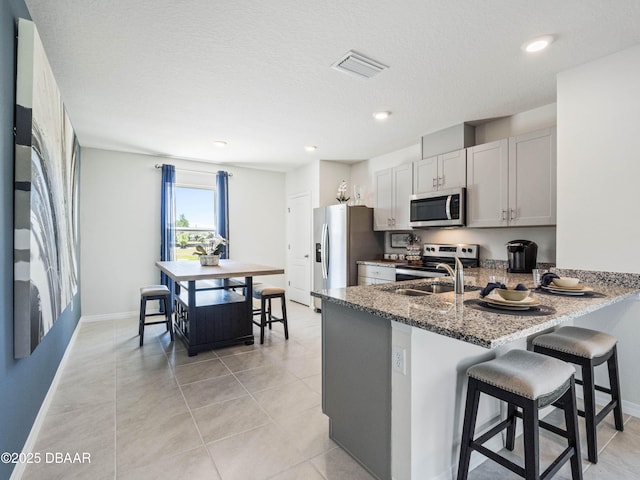 kitchen with white cabinetry, dark stone countertops, stainless steel appliances, a kitchen bar, and kitchen peninsula