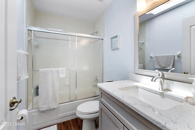 bathroom with toilet, wood finished floors, vanity, and combined bath / shower with glass door