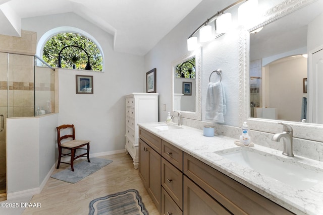 bathroom featuring a shower stall, double vanity, vaulted ceiling, and a sink