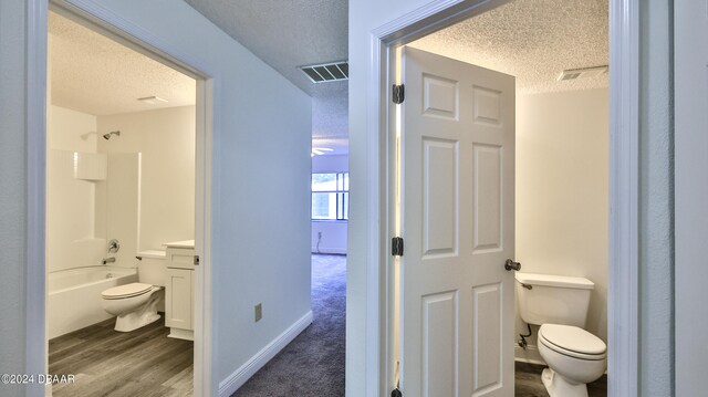 full bathroom with hardwood / wood-style floors, a textured ceiling, toilet, and bathing tub / shower combination