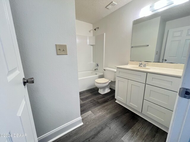 full bathroom with wood-type flooring, toilet, a textured ceiling, shower / bathing tub combination, and vanity