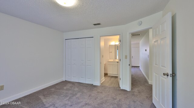 unfurnished bedroom featuring ensuite bathroom, light colored carpet, a textured ceiling, and a closet