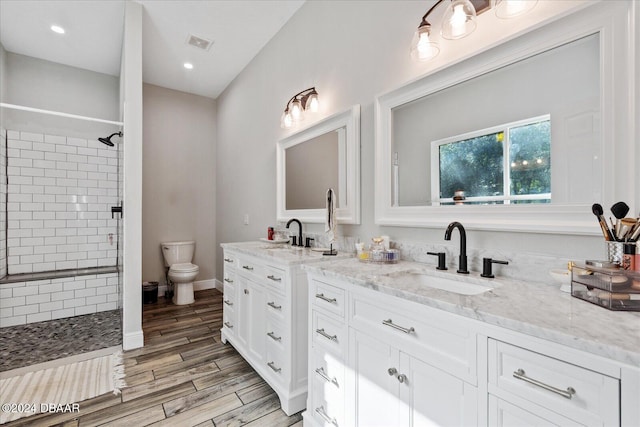 bathroom featuring toilet, vanity, hardwood / wood-style flooring, and a tile shower