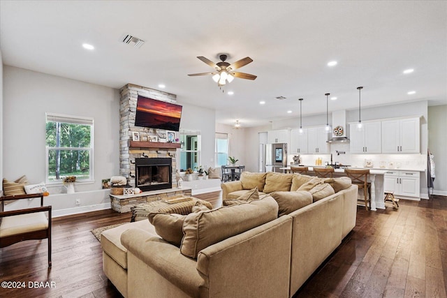 living room with a stone fireplace, ceiling fan, and dark hardwood / wood-style floors