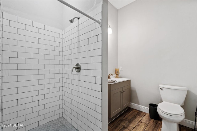 bathroom with toilet, vanity, hardwood / wood-style flooring, and tiled shower