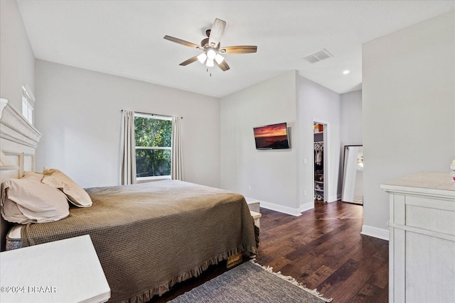 bedroom with a closet, a spacious closet, a fireplace, dark hardwood / wood-style flooring, and ceiling fan