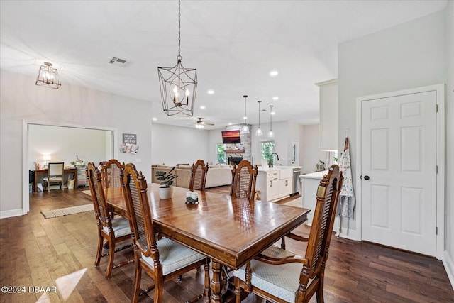 dining area with a fireplace, ceiling fan with notable chandelier, and dark hardwood / wood-style flooring