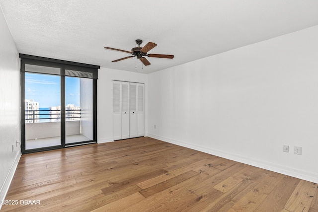 spare room with a view of city, a ceiling fan, a textured ceiling, light wood-type flooring, and baseboards