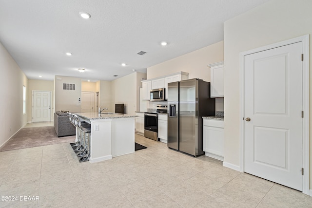 kitchen with stainless steel appliances, a center island with sink, light stone counters, a kitchen breakfast bar, and white cabinets