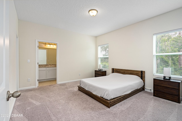 bedroom with ensuite bathroom, light colored carpet, and a textured ceiling