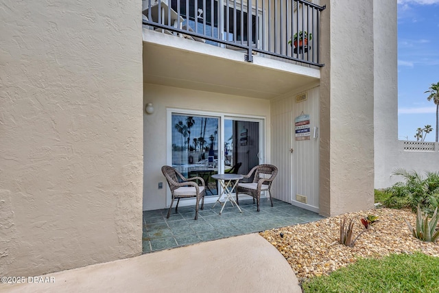 property entrance featuring stucco siding, a patio area, and a balcony