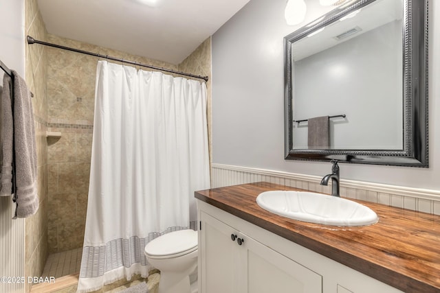 full bath with wainscoting, vanity, toilet, visible vents, and tiled shower