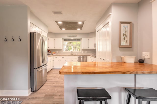 kitchen with a peninsula, light wood-style floors, recessed lighting, white cabinetry, and stainless steel appliances