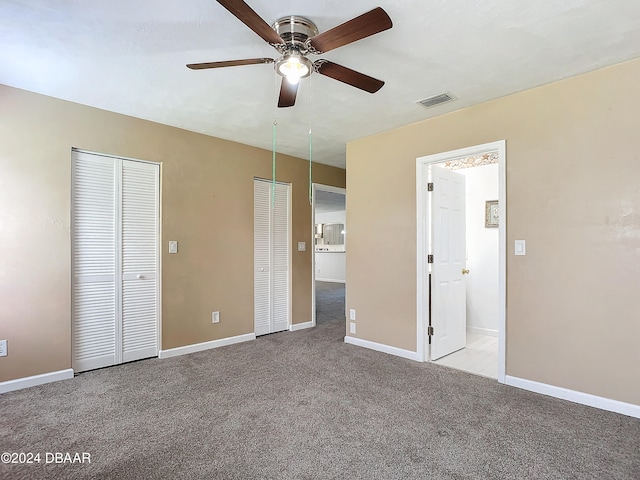 unfurnished bedroom featuring multiple closets, light carpet, and ceiling fan