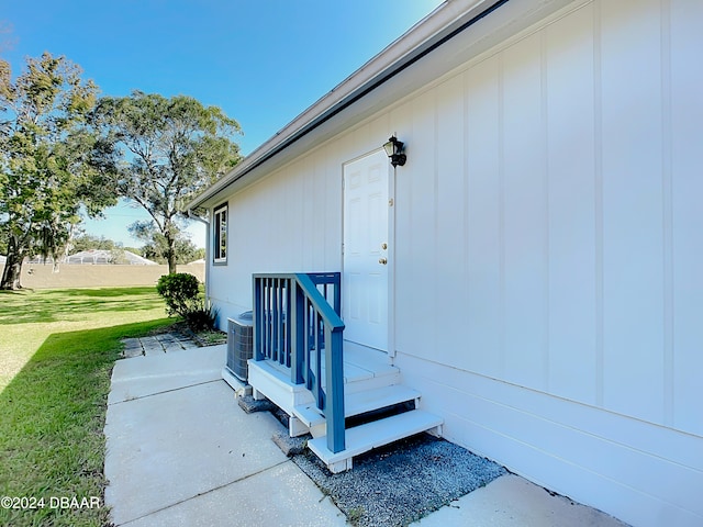 view of exterior entry featuring central air condition unit and a lawn