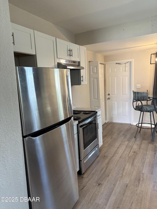 kitchen with light wood-type flooring, under cabinet range hood, white cabinetry, and appliances with stainless steel finishes