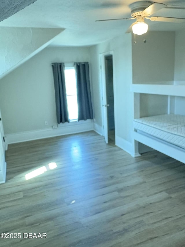 unfurnished living room with a ceiling fan, baseboards, and wood finished floors