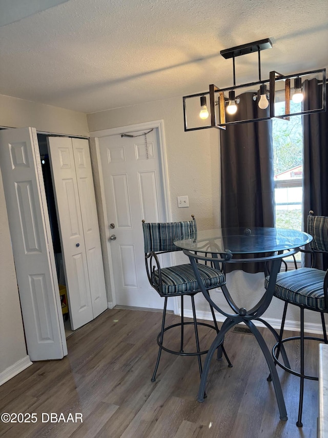 dining space with an inviting chandelier, a textured ceiling, baseboards, and wood finished floors