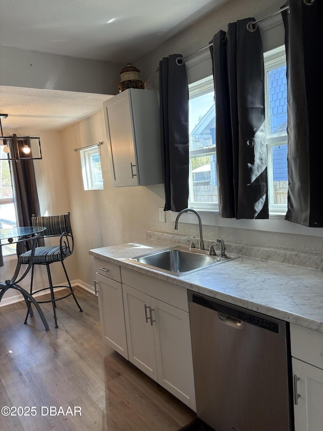 kitchen with wood finished floors, a sink, white cabinetry, light countertops, and stainless steel dishwasher