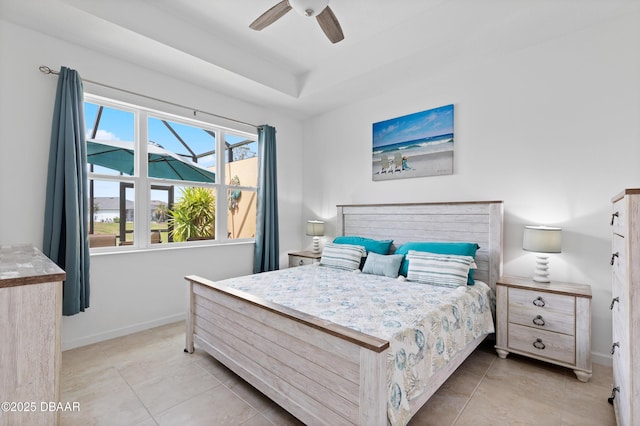 bedroom with light tile patterned floors, a tray ceiling, baseboards, and ceiling fan