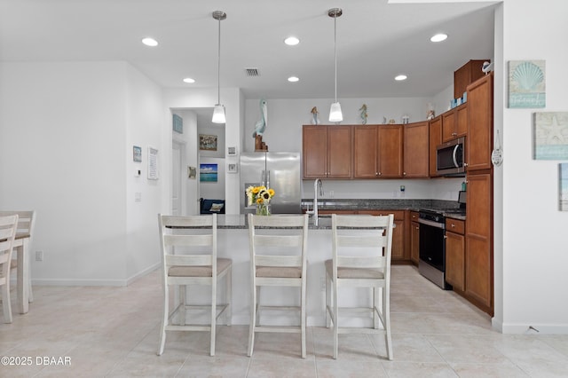 kitchen with visible vents, a breakfast bar, a kitchen island with sink, hanging light fixtures, and appliances with stainless steel finishes