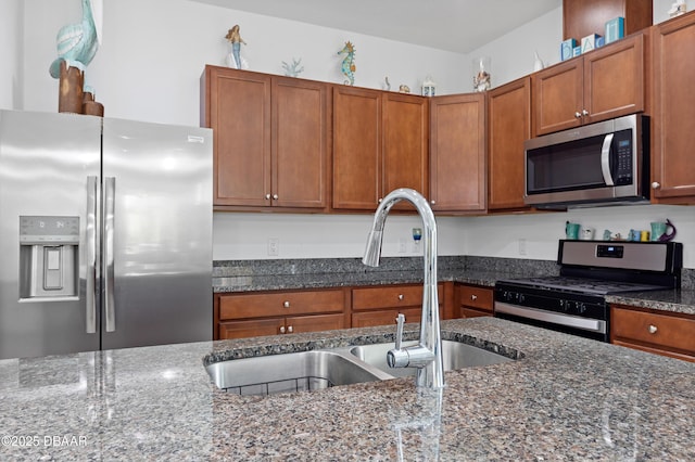 kitchen with a sink, appliances with stainless steel finishes, brown cabinetry, and dark stone countertops