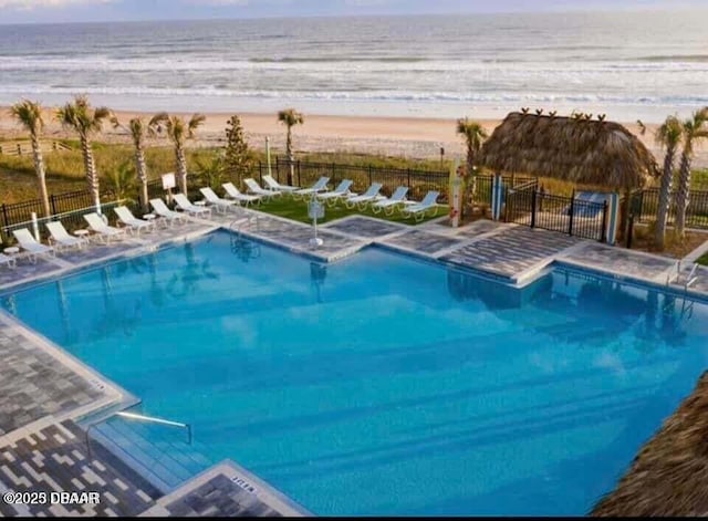 community pool with a beach view, a water view, and fence