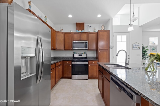 kitchen with brown cabinetry, appliances with stainless steel finishes, dark stone counters, and a sink